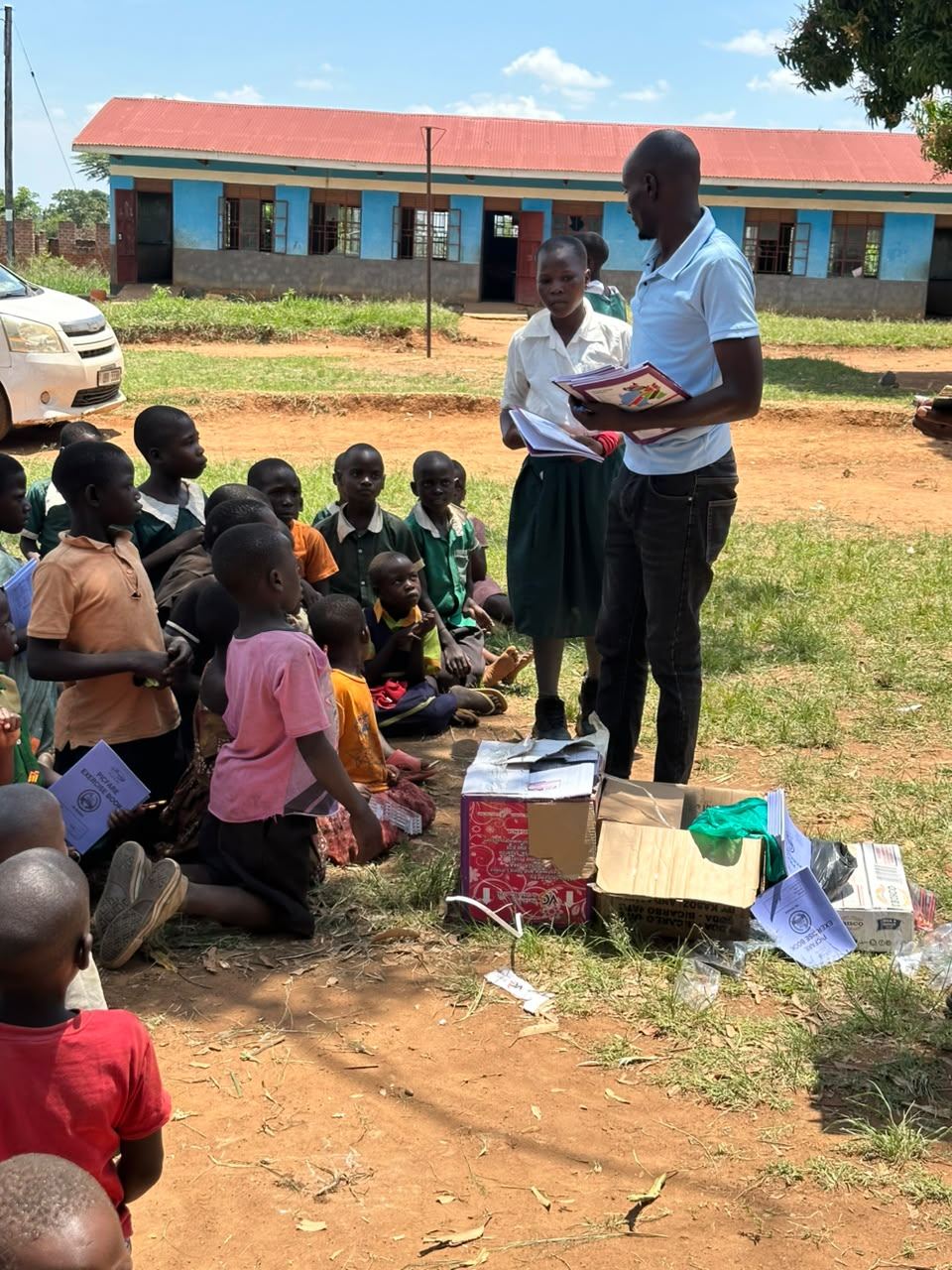 Children gathered on the grass as books are handed out
