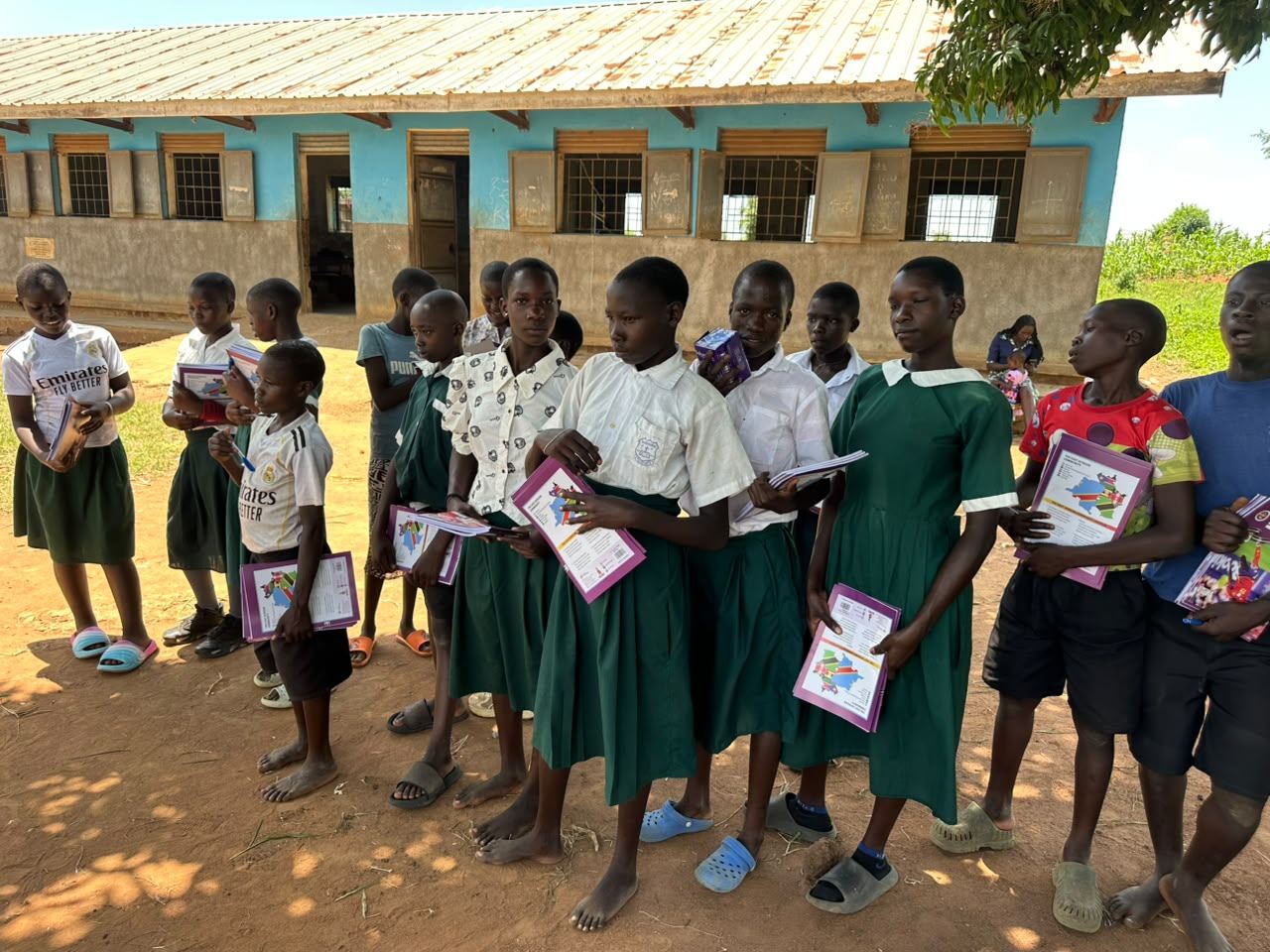 Pupils in school uniforms holding new exercise books outside their classroom in Uganda
